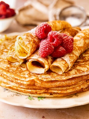 Blini stacked on a plate, topped with raspberries.