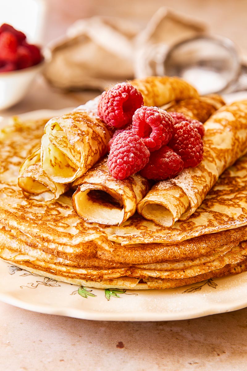 Blini stacked on a plate, topped with raspberries. 