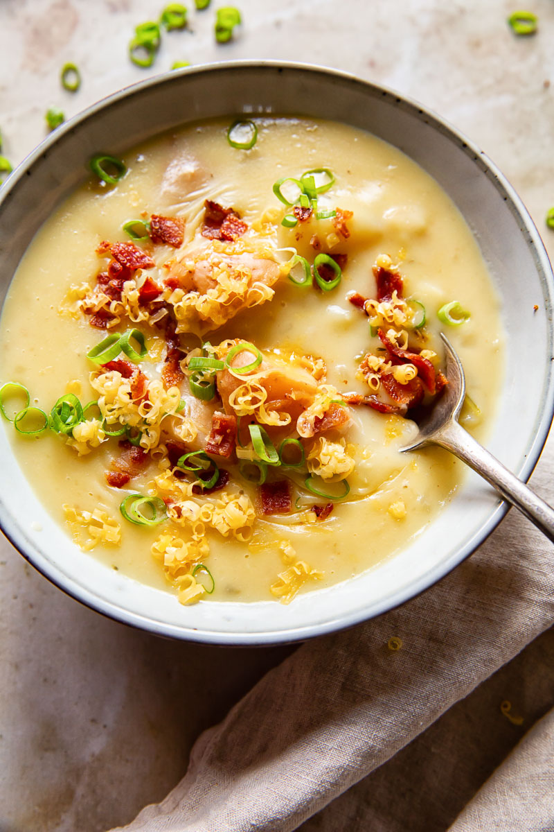 potato soup topped with green onions, bacon and grated cheese in grey bowl with a spoon