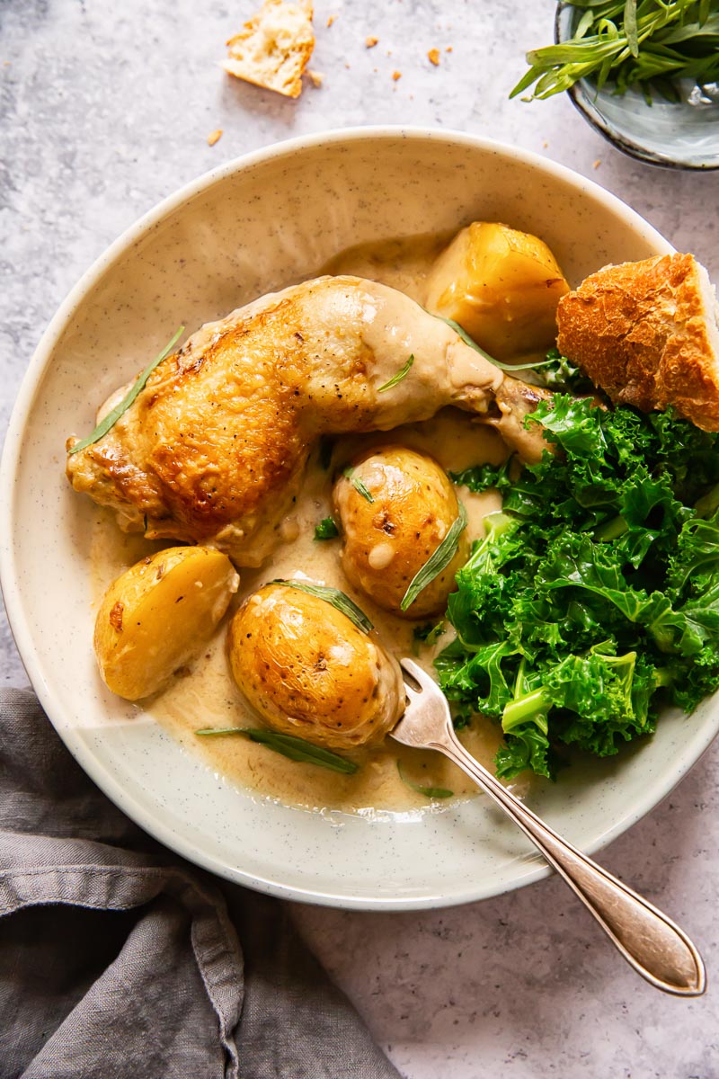 chicken leg and potatoes with cream sauce poured over in a bowl. A side of cooked kale. 