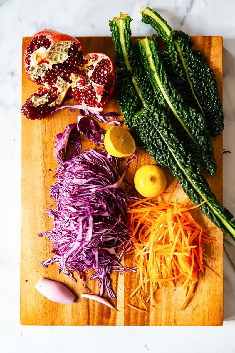 Sliced red cabbage, kale, carrots, pomegranate and shallots on cutting board 