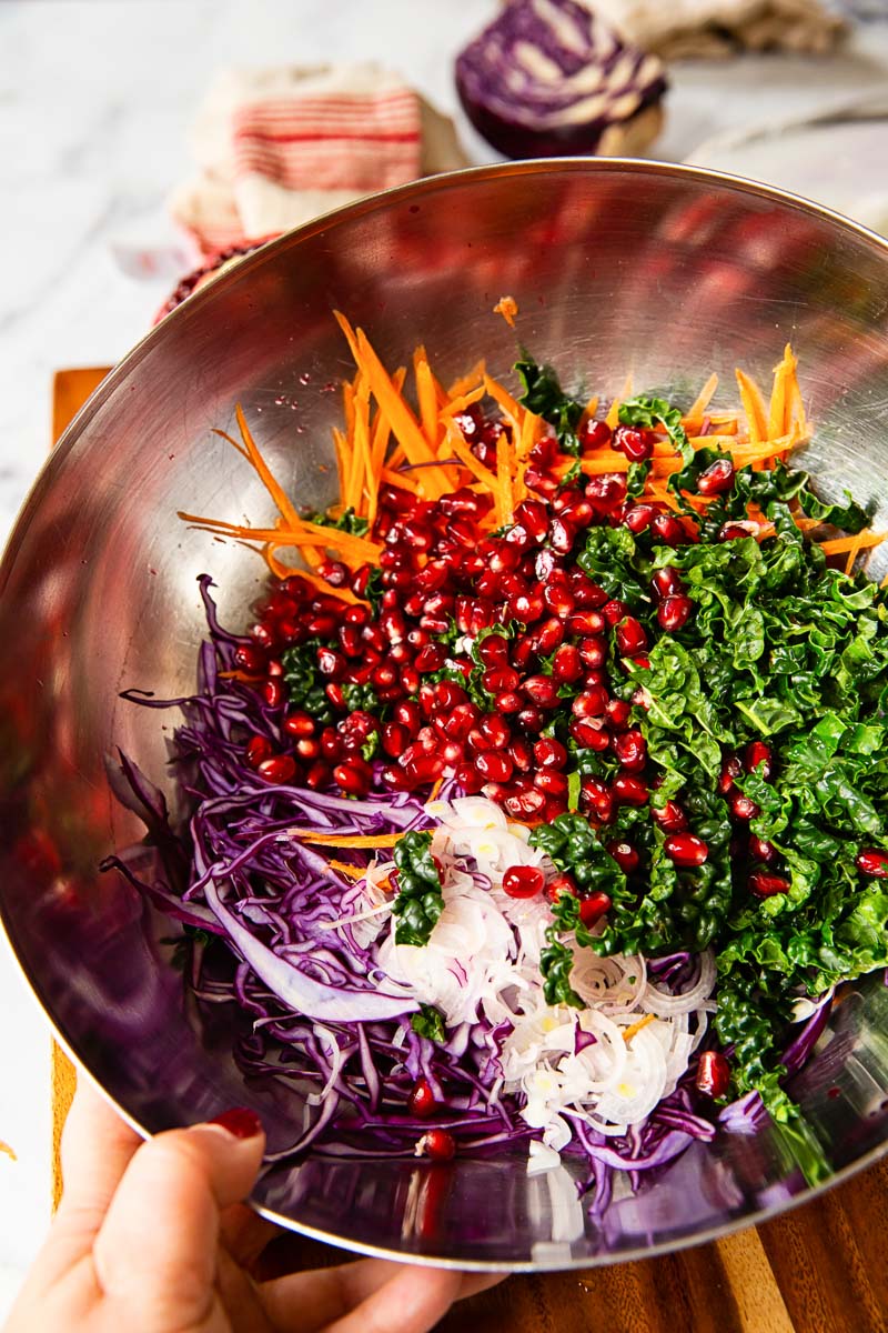 Sliced red cabbage, carrots, kale and pomegranate seeds in a bowl