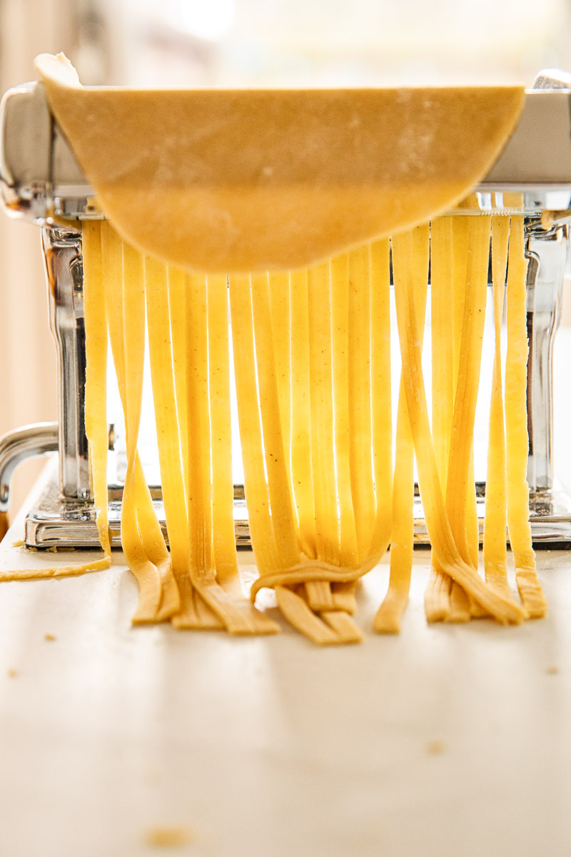 fresh pasta dough being cut into fettuccine