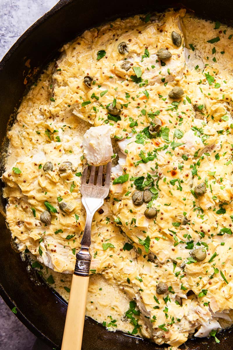 fish under a creamy sauce sprinkled with fresh chopped parsley in cast iron skillet