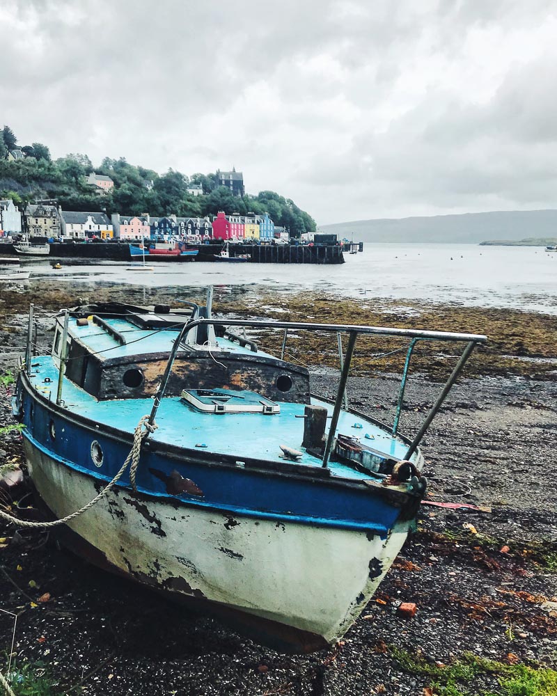 abandoned boat on shore with a town in the background