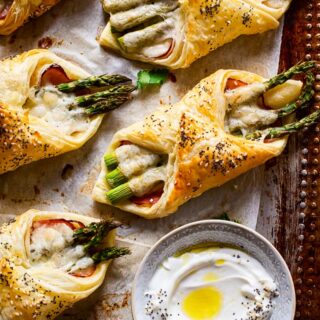 cheese and asparagus puff pastry pockets on baking sheet a small dish with dip