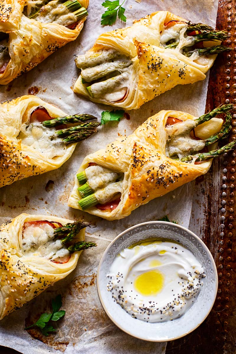 cheese and asparagus puff pastry pockets on baking sheet a small dish with dip