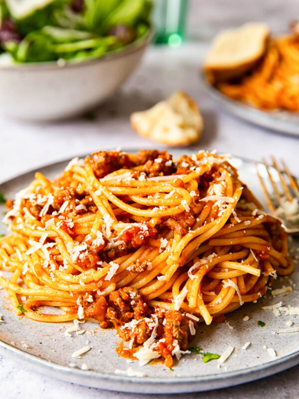 spaghetti bolognese on grey plate with salad in the background