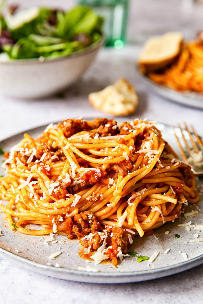 spaghetti bolognese on grey plate with salad in the background