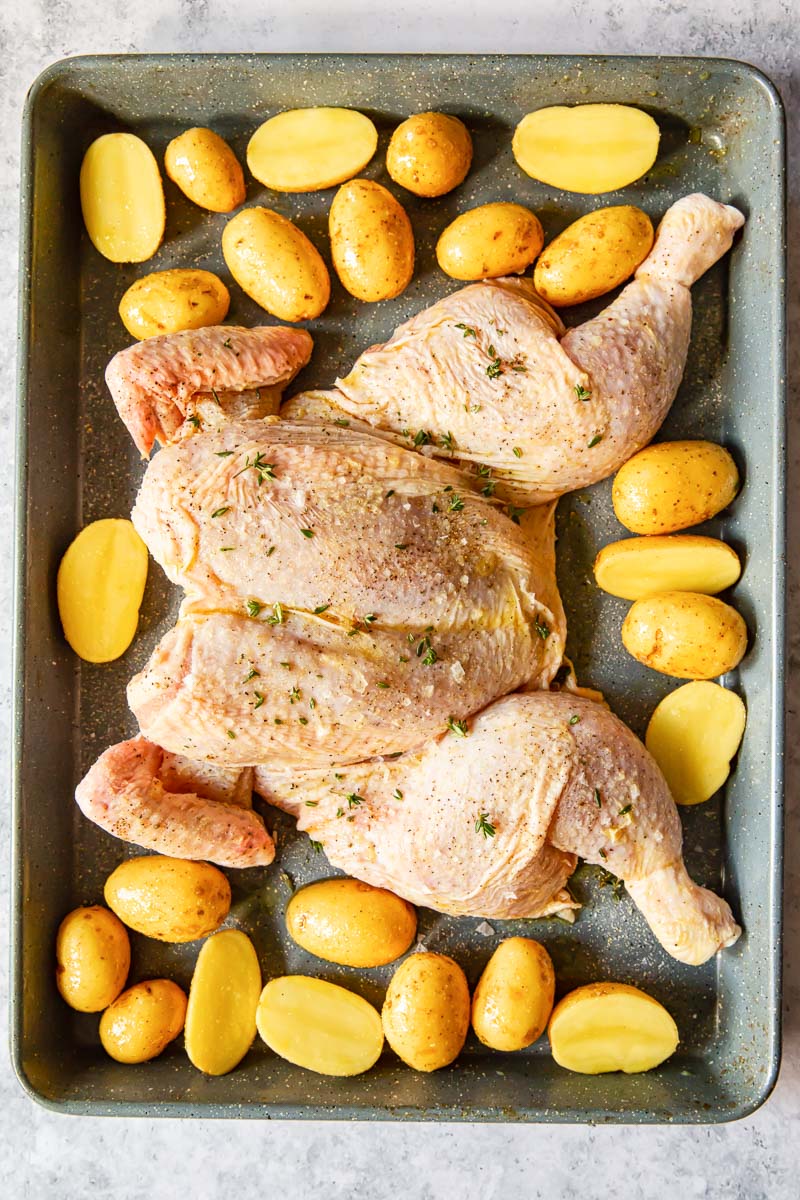 uncooked butterflied chicken and potatoes on a pan