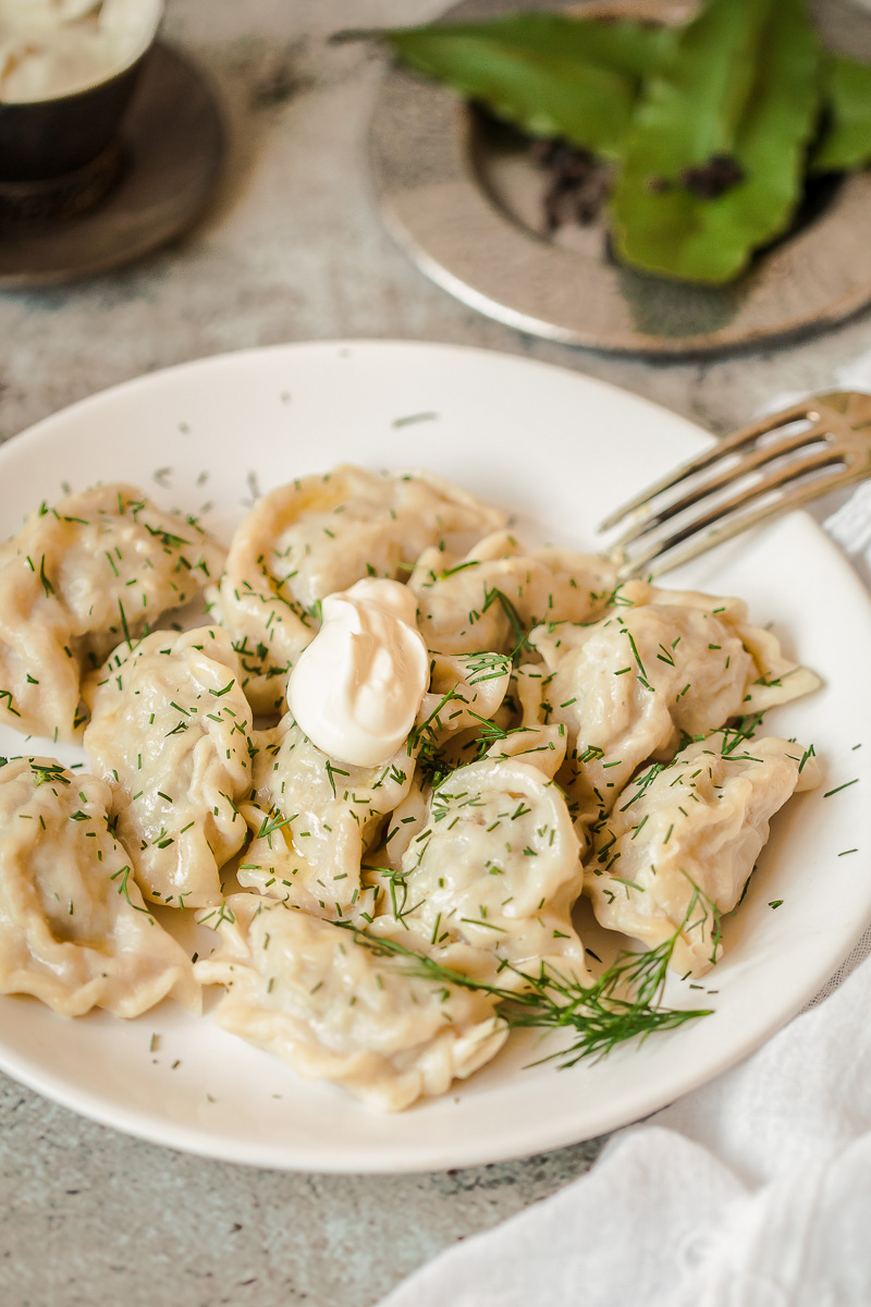 pelmeni with dill and sour cream on a plate