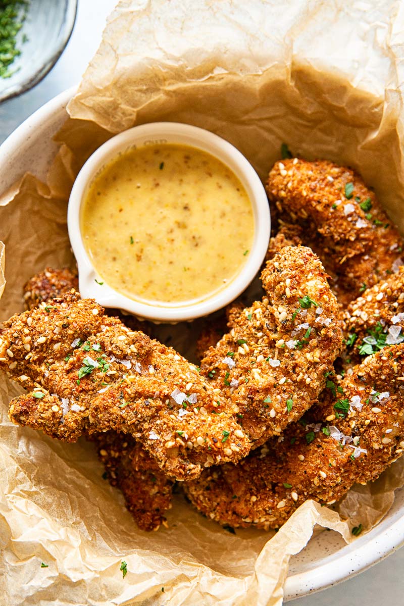 chicken tenders, honey mustard sauce in a small dish inside a wax paper lined bowl