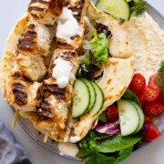 chicken souvlaki skewers on top of pita bread filled with hummus and vegetables