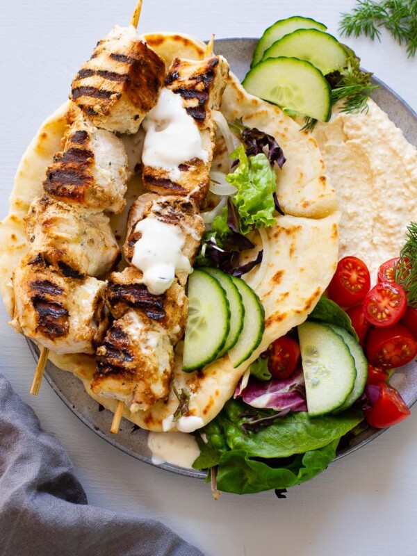 chicken souvlaki skewers on top of pita bread filled with hummus and vegetables