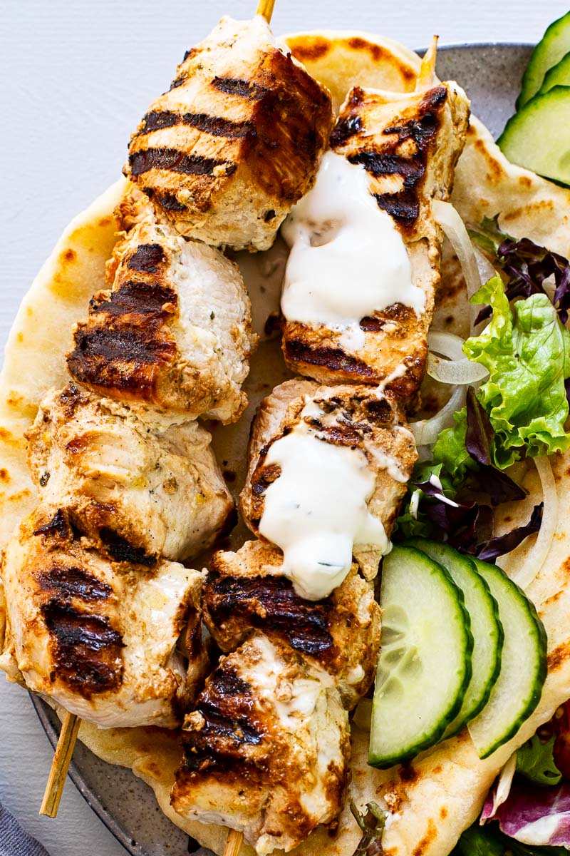 two chicken skewers on top of flatbread drizzled with yogurt