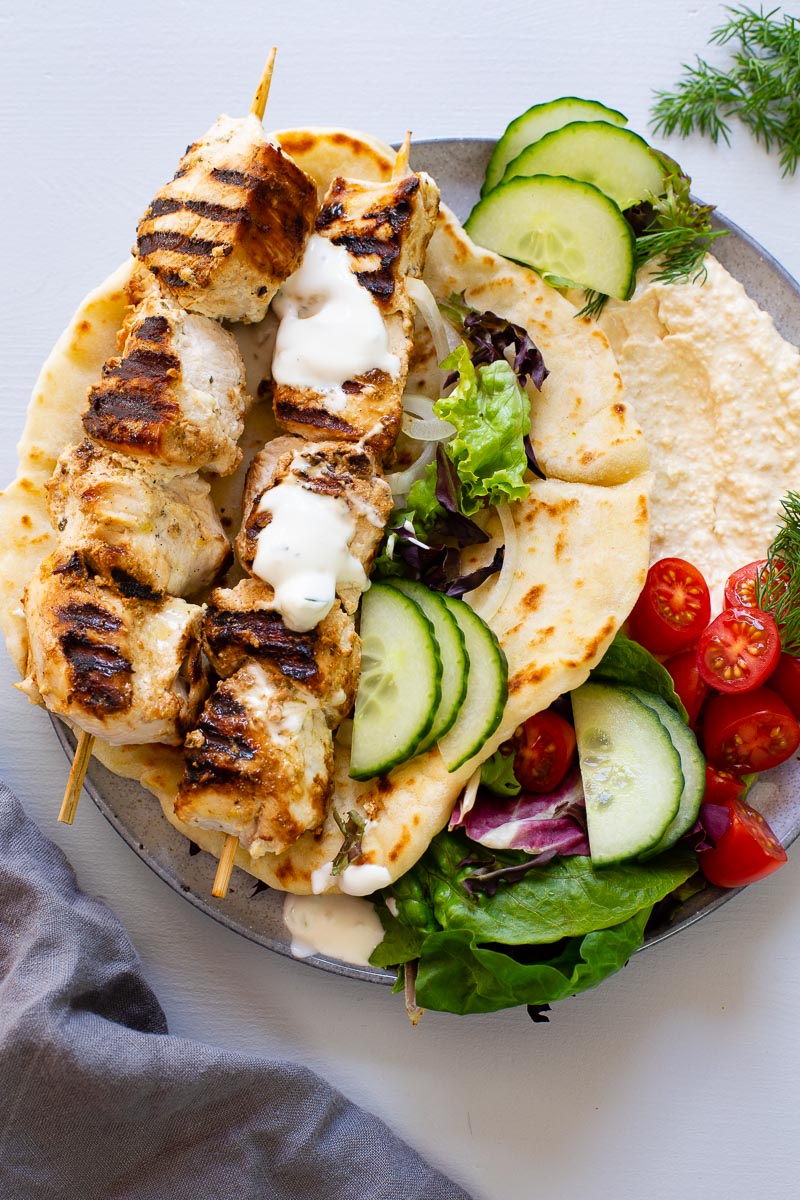 chicken souvlaki skewers on top of pita bread filled with hummus and vegetables