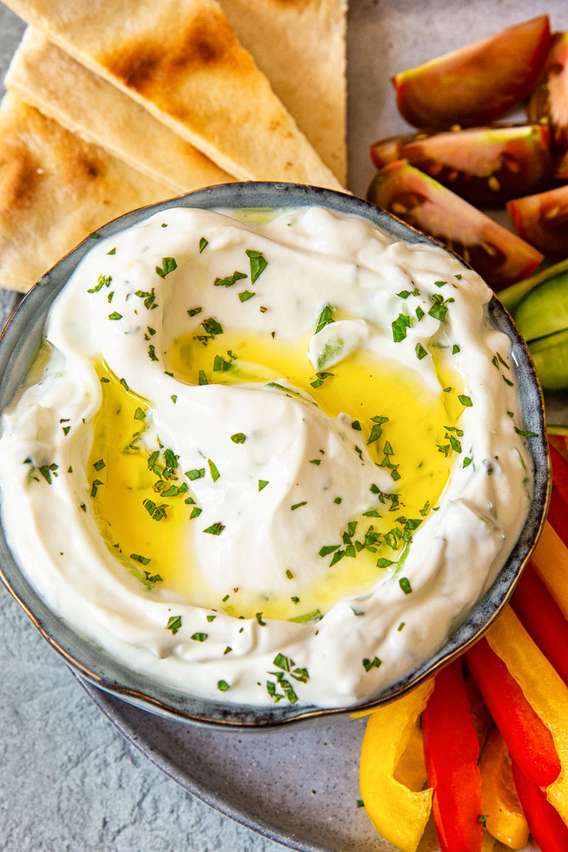 yogurt and cucumber dip sprinkled with fresh mint on a platter with pita and cut up vegetables