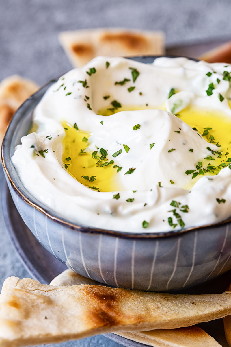 Tzatziki sauce in blue bowl, pita bread around it.