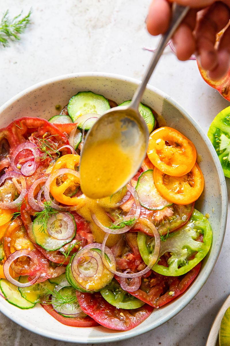 cucumber and tomato salad with a spoonful of salad dressing being poured on it