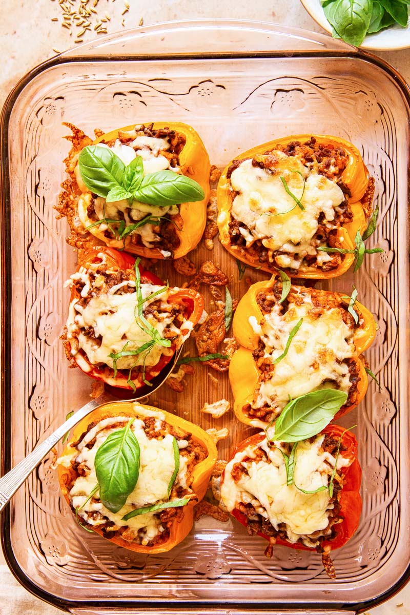 stuffed bell peppers topped with melted cheese and fresh basil in a pan 