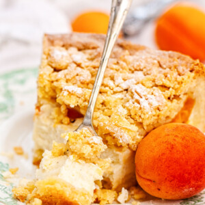 Apricot cheesecake with crumb topping on a plate with a fresh apricot next to it