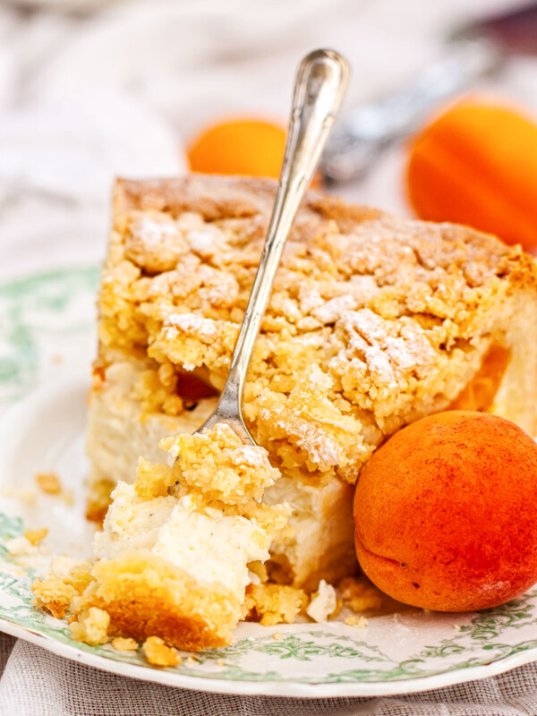 Apricot cheesecake with crumb topping on a plate with a fresh apricot next to it
