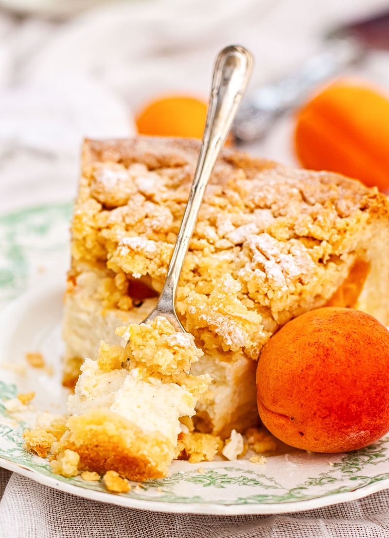 Apricot cheesecake with crumb topping on a plate with a fresh apricot next to it
