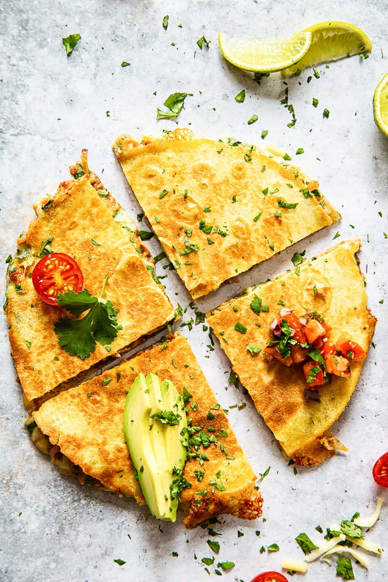 cheese quesadilla cut into quarters and topped with sliced avocado and pico de gallo on grey surface