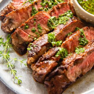 sliced rib eye steak with herb sauce on grey plate