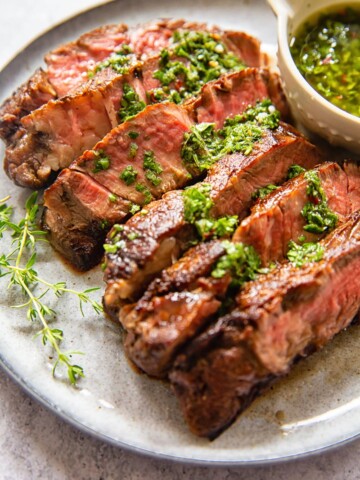 sliced rib eye steak with herb sauce on grey plate