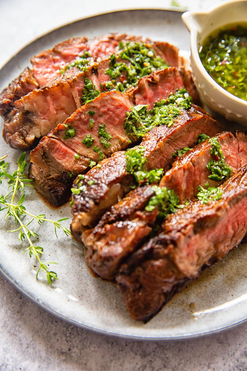 sliced rib eye steak with herb sauce on grey plate