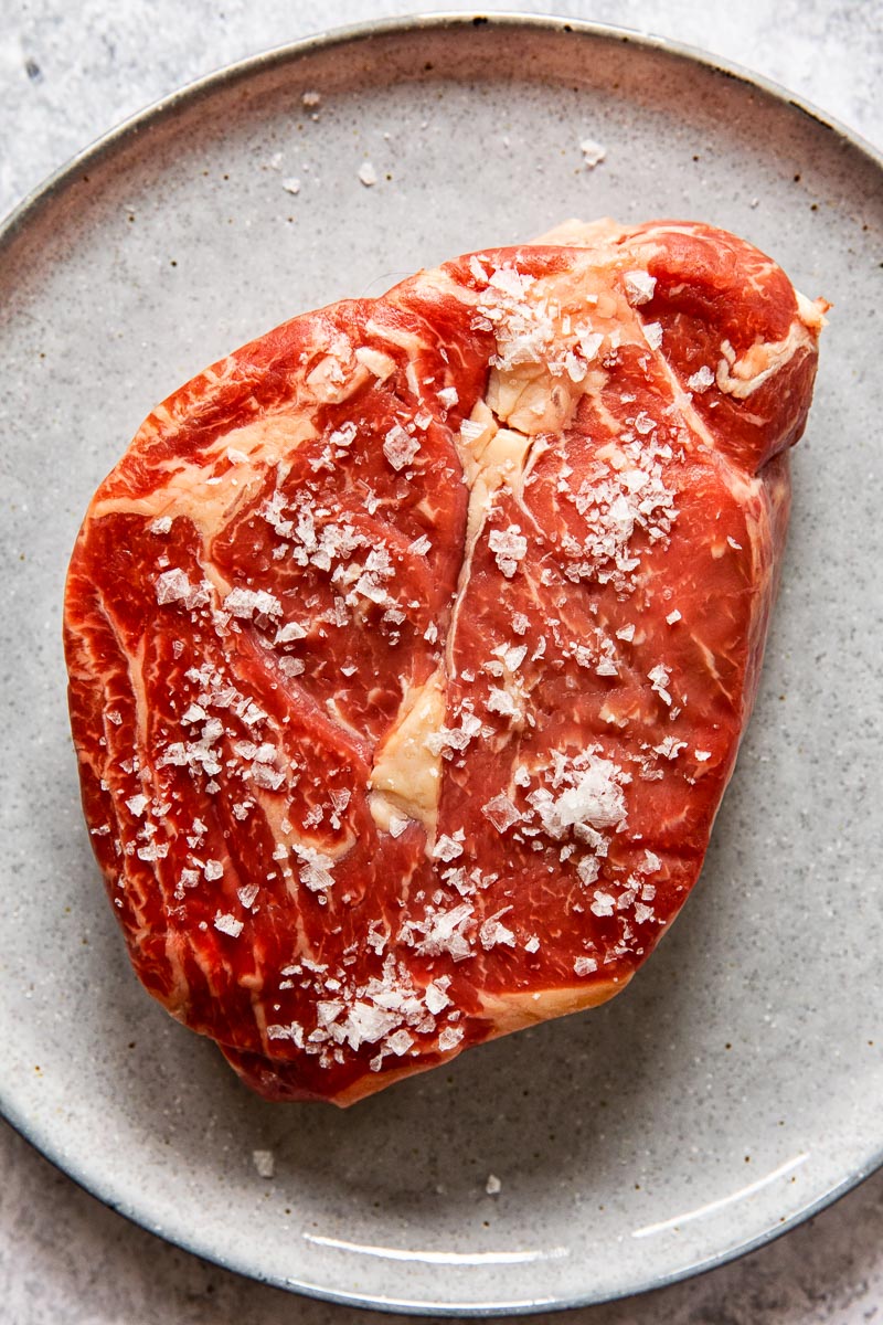 raw ribeye steak sprinkled with flaked salt on grey plate