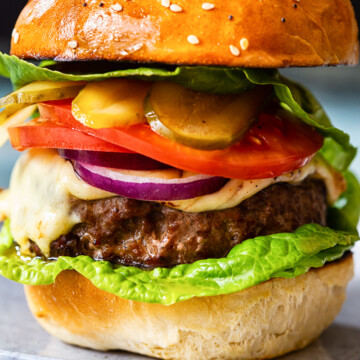 homemade burger with cheese, tomatoes, onions and pickles on grey plate closeup