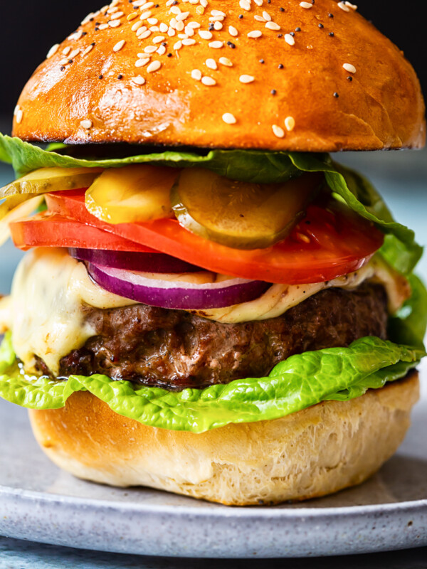 homemade burger with cheese, tomatoes, onions and pickles on grey plate closeup