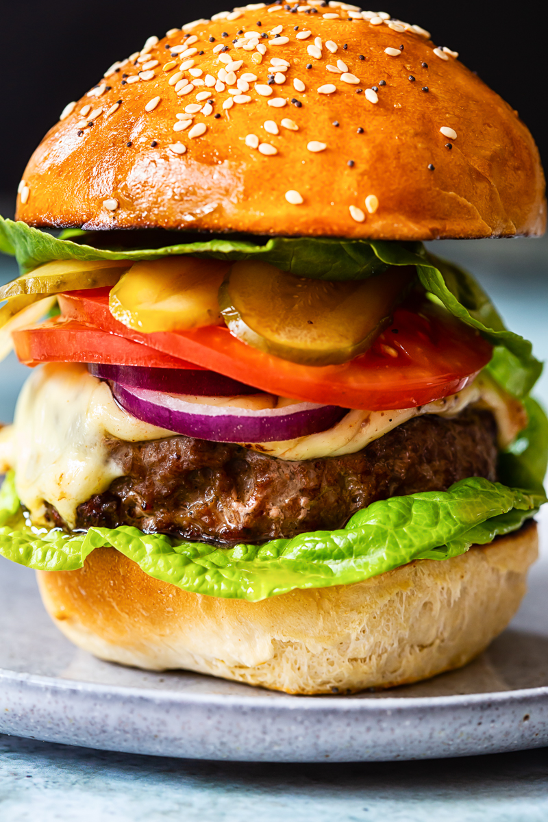 homemade burger with cheese, tomatoes, onions and pickles on grey plate closeup