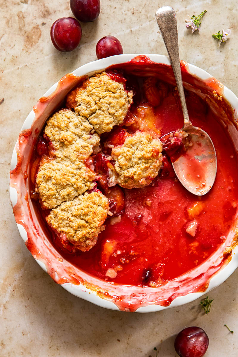 a round pan filled with half eaten plum cobbler and a spoon