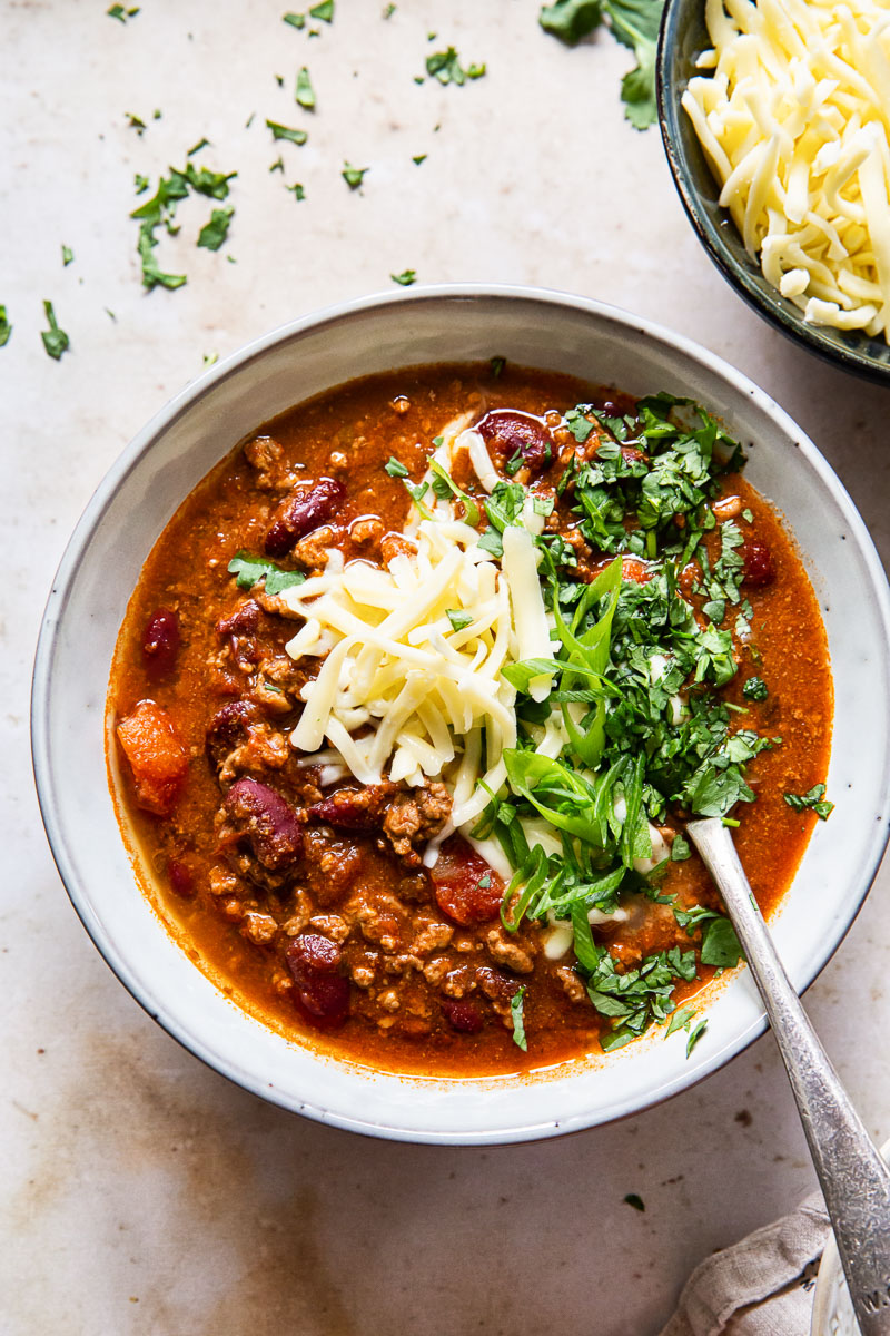 chili in grey bowl topped with grated cheese, sliced onions and cilantro