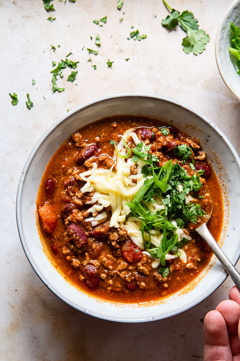 a bowl of chili with a hand holding a spoon dipped in the dish