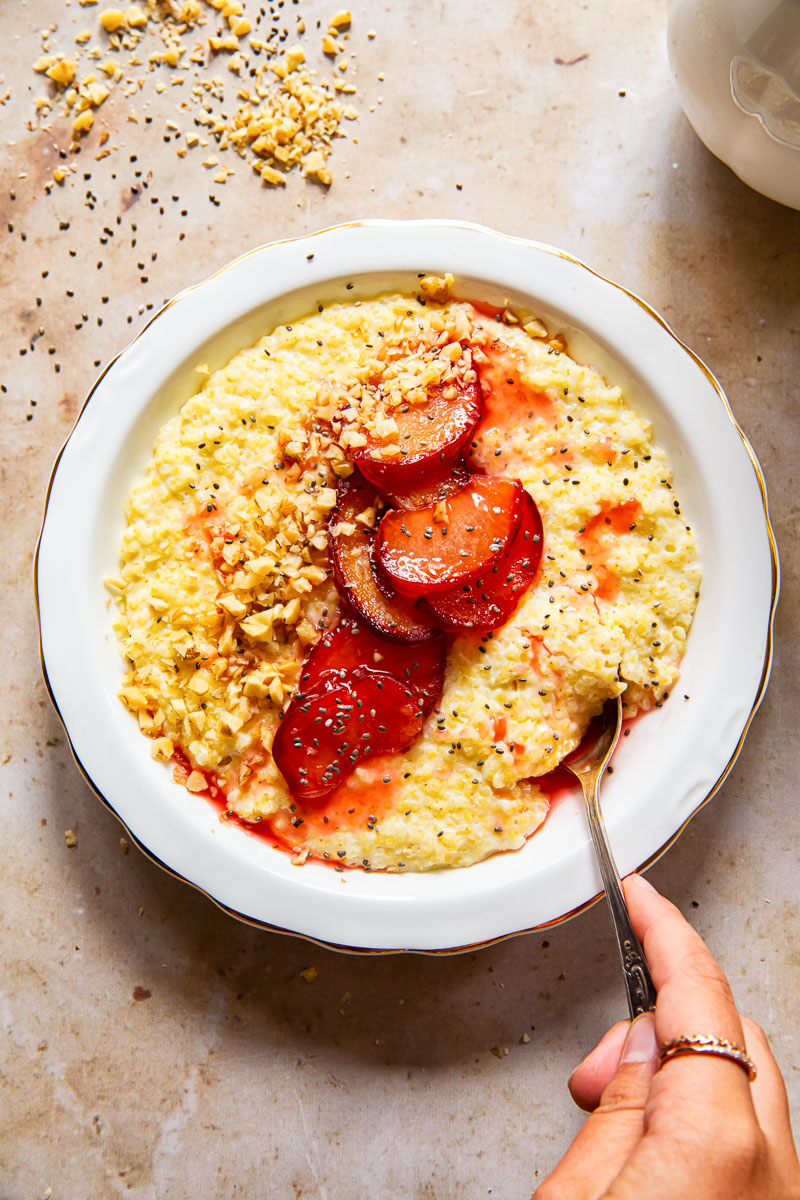 top down view of a bowl of porridge with a hand reaching in with a spoon