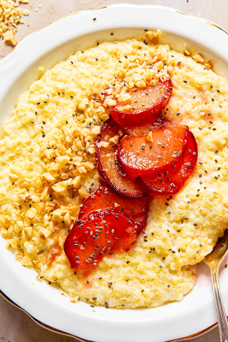 closeup image of millet porridge topped with plums, walnut and chia seeds