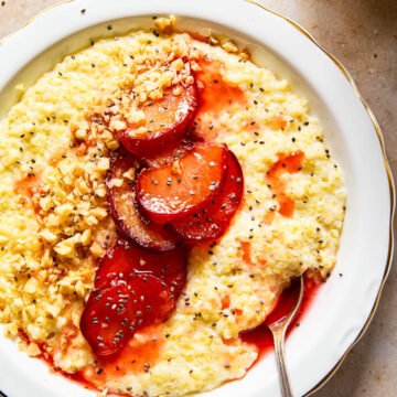 millet porridge in white bowl topped with cooked plums, walnut and chia seeds