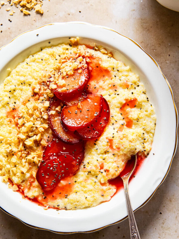 millet porridge in white bowl topped with cooked plums, walnut and chia seeds