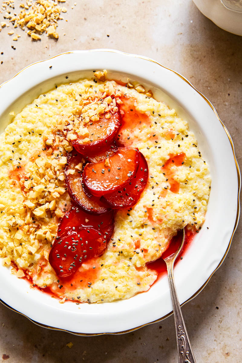 millet porridge in white bowl topped with cooked plums, walnut and chia seeds