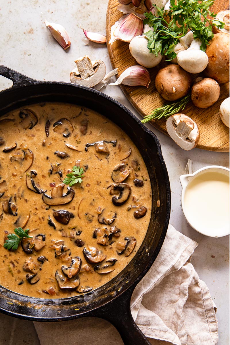 mushroom sauce on black pan, raw white and brown mushroom on cutting board, cream