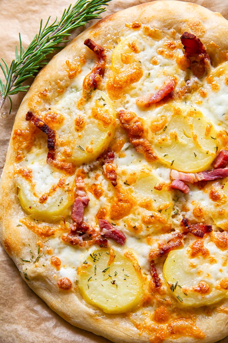 potato and pancetta pizza on parchment paper, rosemary sprig next to it