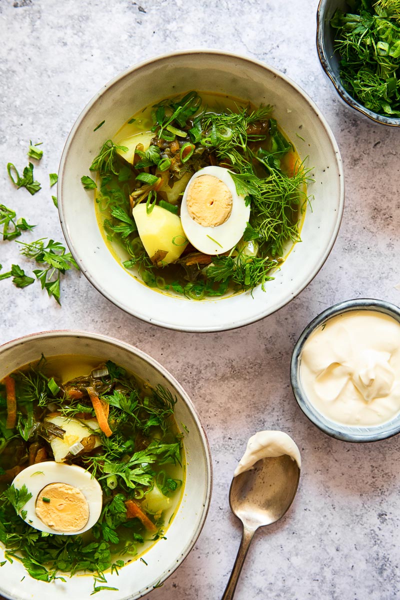 two grey bowl filled with sorrel soup and topped with greens and hard boiled egg on grey background