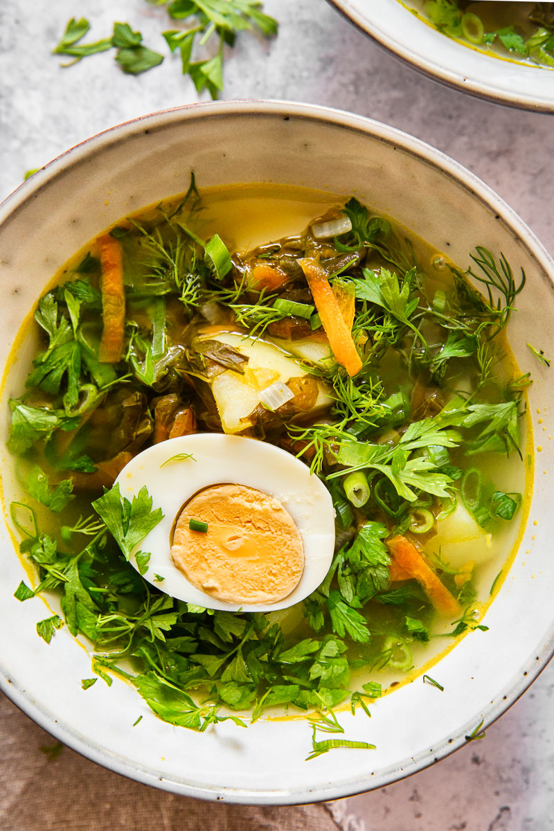 green borscht topped with parsley and dill and a hard boiled egg half