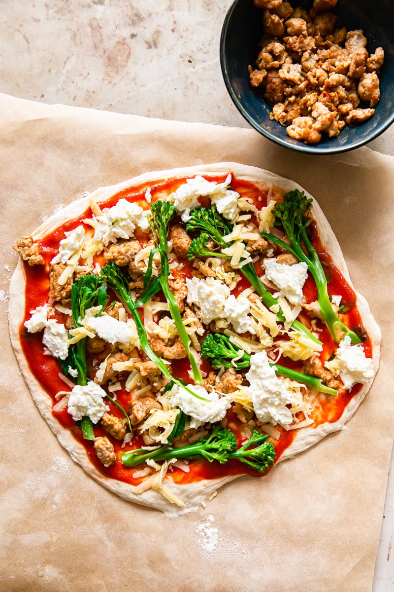 unbaked pizza crust topped with sausage, broccoli and mozzarella