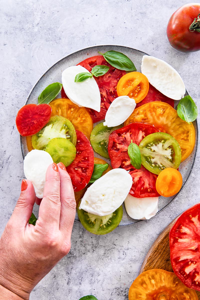 a mozzarella slice is being added to the plate of the Caprese salad