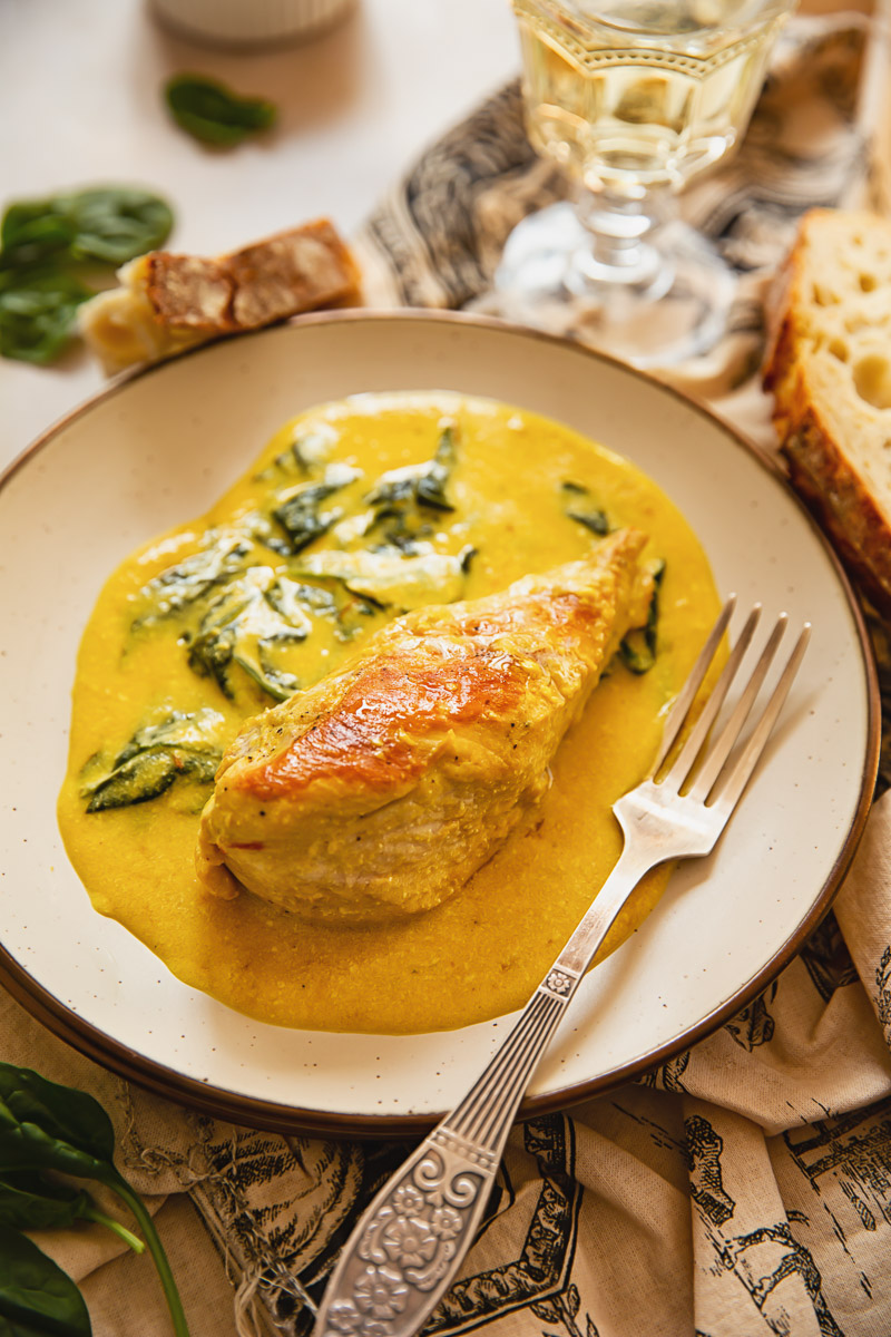 chicken breast with tuscan cream sauce and spinach on beige plate, fork and glass of white wine